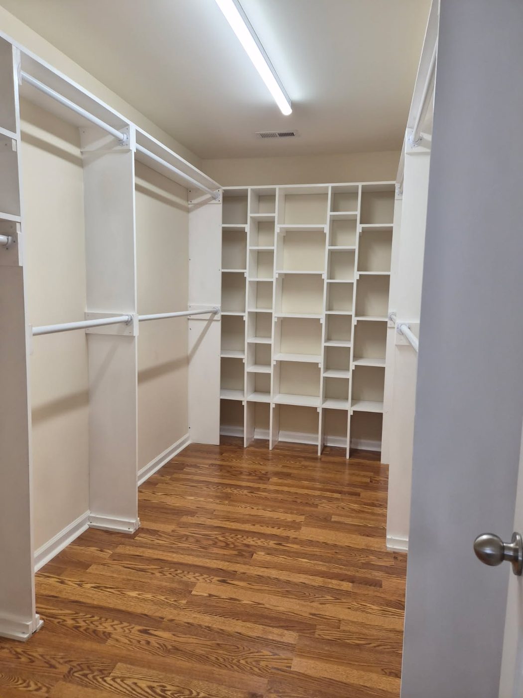 Walk in closet built out with white shelving, cubbies and hanging rods over hardwood flooring