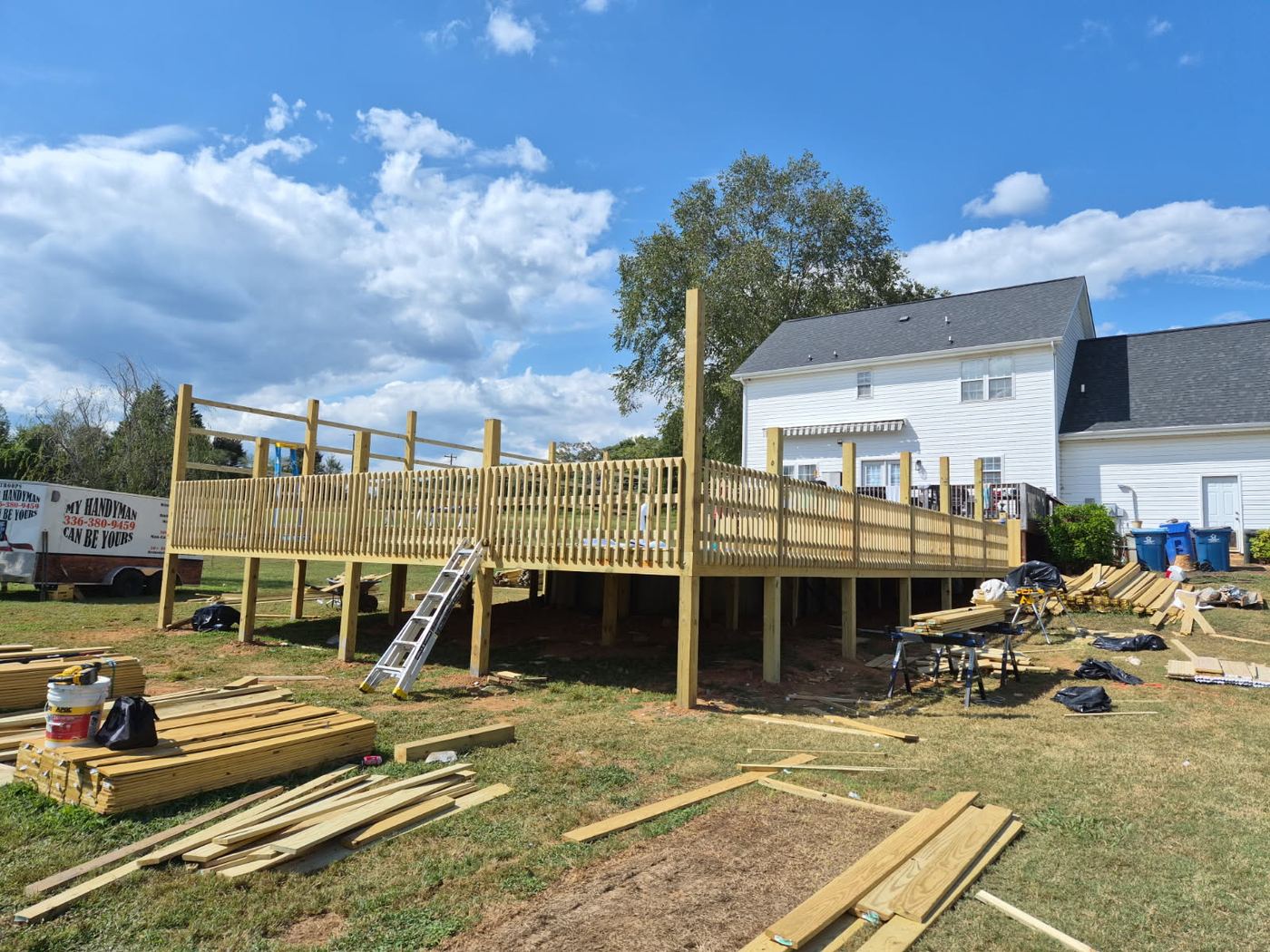 Large elevated deck under construction behind a two story Alamance County home, picket railing installed and framing lumber stacked on the lawn