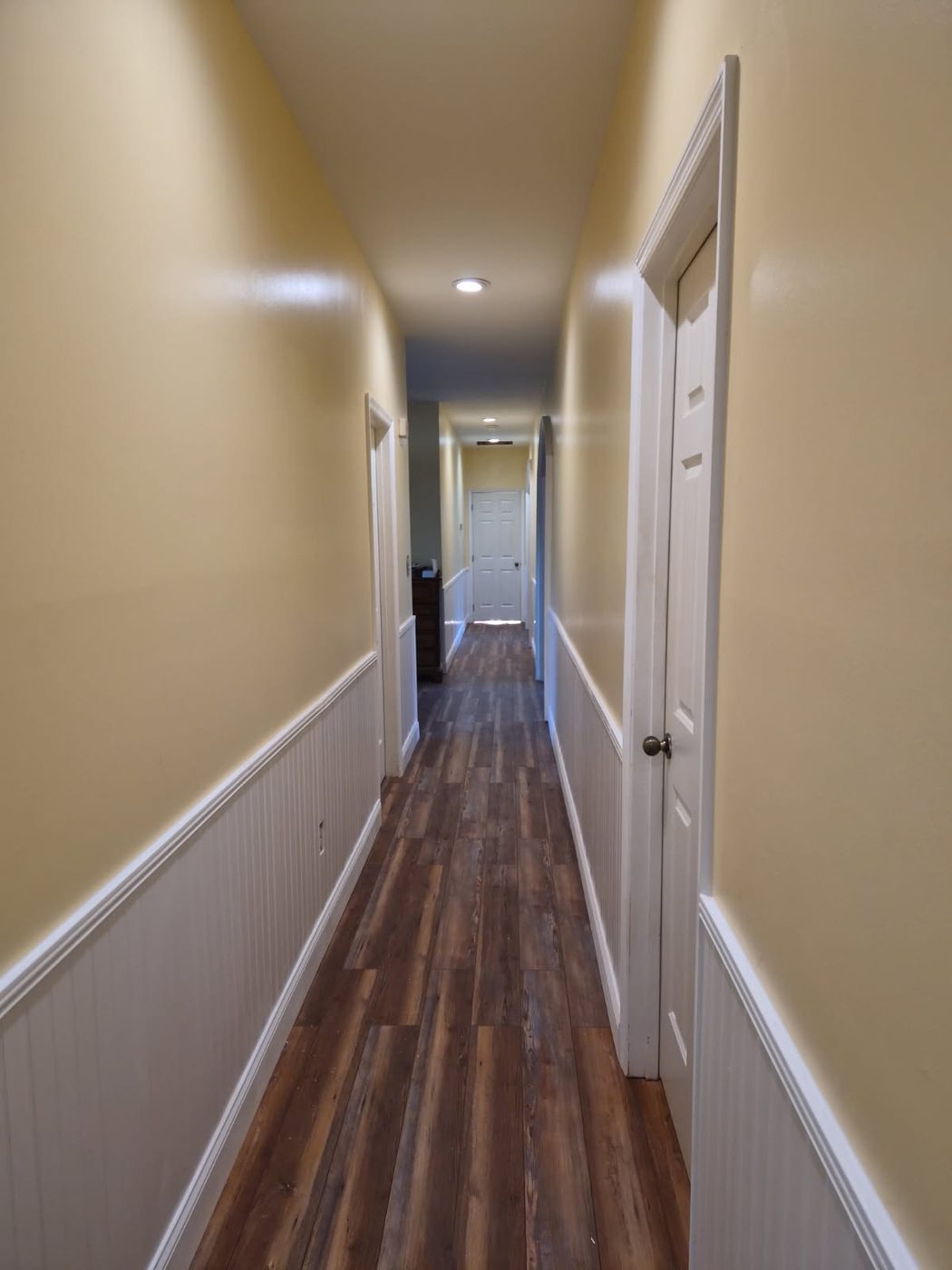Finished hallway with new wood look flooring, white beadboard wainscot, trim and freshly painted walls in a Burlington NC home