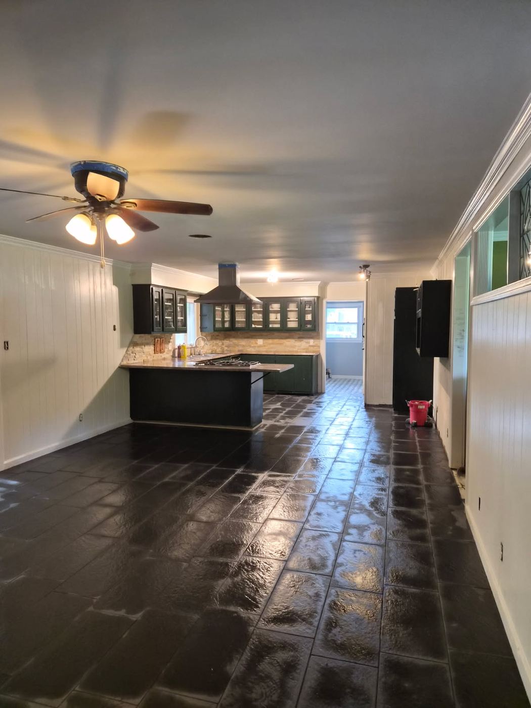 The same kitchen and living room finished with a smooth ceiling after texture removal, dark tile floor, repainted cabinets and white panelled walls