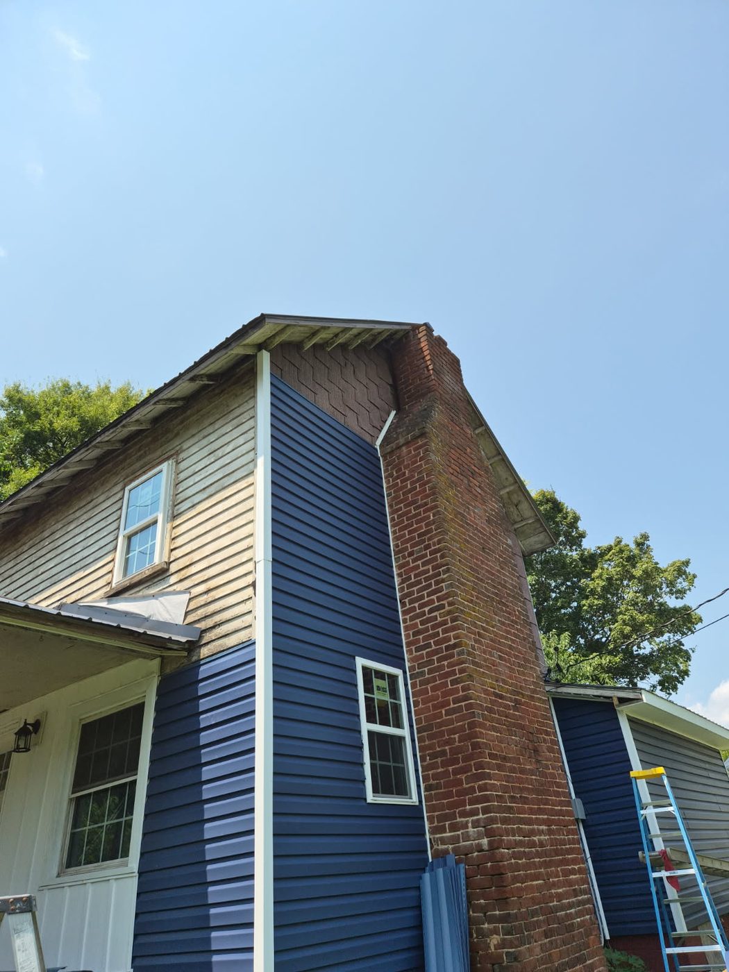 Blue vinyl siding and new white replacement windows being installed over old wood siding on a two story house in Alamance County NC